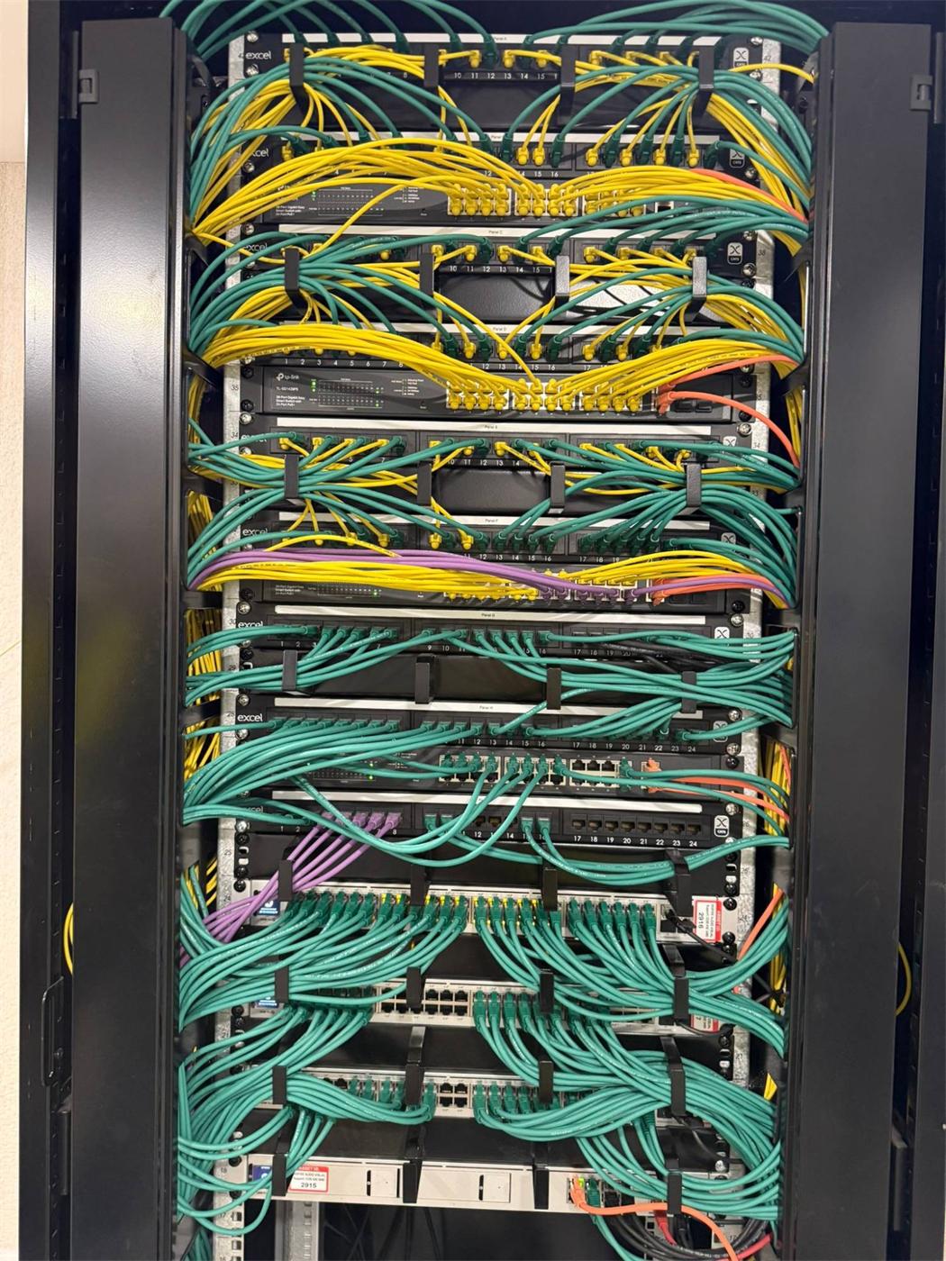 Comms cabinet with colour-coded patch leads dressed through cable managers between patch panels and PoE switches